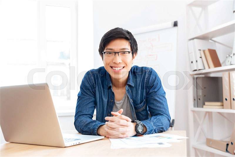 Portrait of cheerful asian young businessman working with laptop on workplace , stock photo