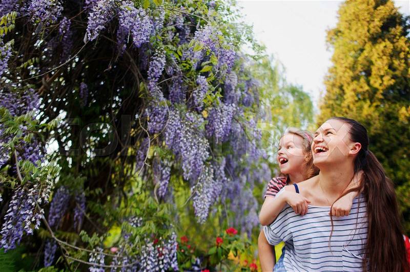 Mother and daughter walking in the summer park. Young woman holding a little girl on his shoulders. They are surrounded by blooming plants. The faces of delight, tenderness and love, stock photo