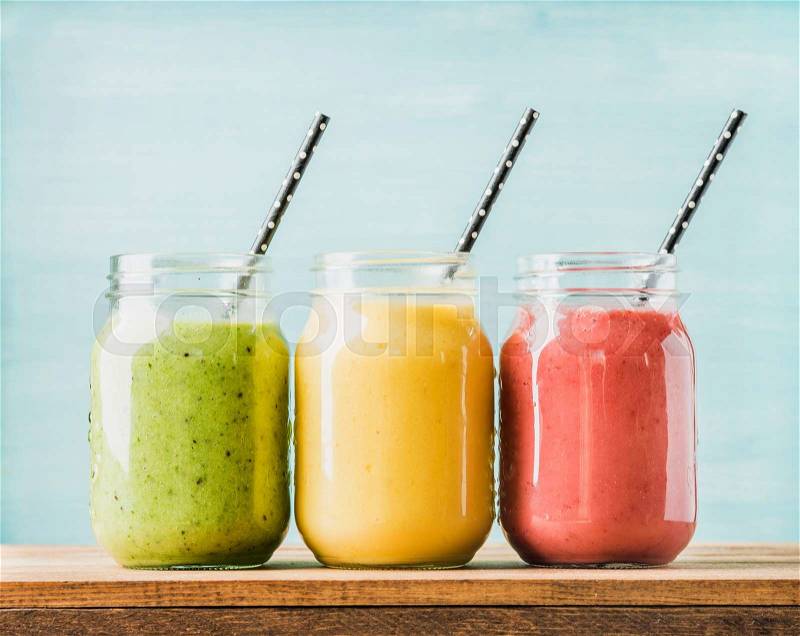 Freshly blended fruit smoothies of various colors and tastes in glass jars. Yellow, red, green. Turquoise blue background, stock photo