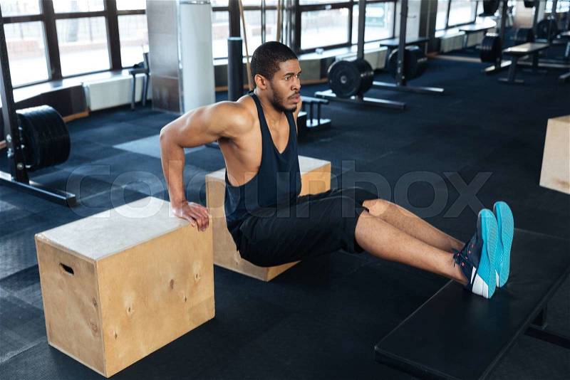 Strong fitness man pumps biceps using training apparatus in the gym, stock photo