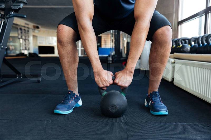 Cropped image of a bodybuilder with kettlebell in a gym, keep kettlebell with two hands, stock photo