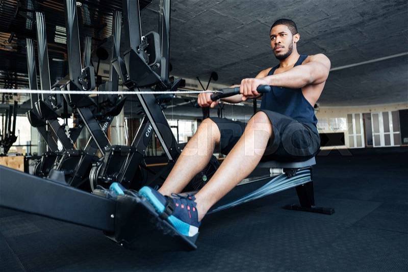 Muscular fit man using rowing machine at gym, stock photo