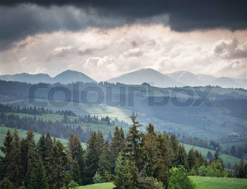 Mountains and storm clouds in the morning. A ray of sunlight shining through the clouds on a small portion of the mountain slope, stock photo