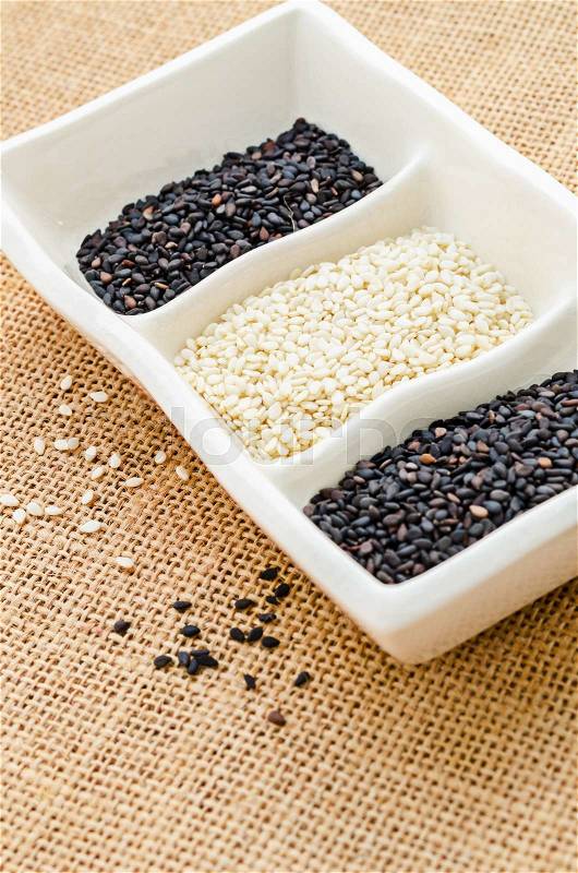 White sesame and black sesame in white cup on sack background, stock photo