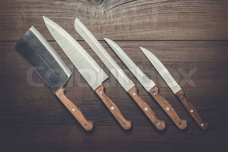 Five kitchen knifes on the brown wooden table, stock photo