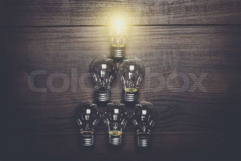Glowing bulb leadership concept on brown wooden background, stock photo