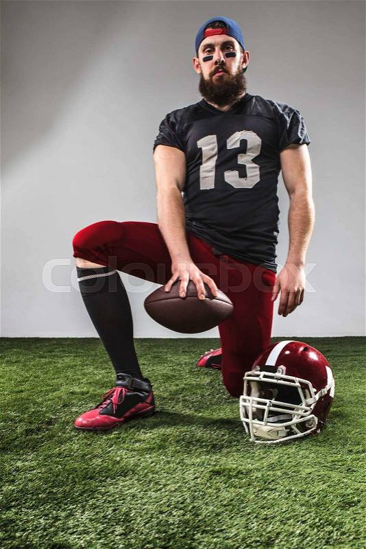 The american football player with ball posing on green grass and gray background, stock photo