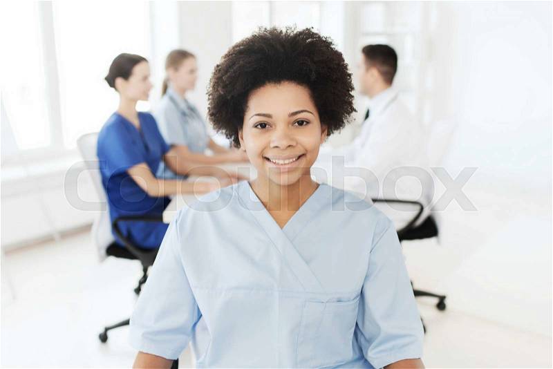 Clinic, profession, people and medicine concept - happy african american female doctor or nurse over group of medics meeting at hospital, stock photo