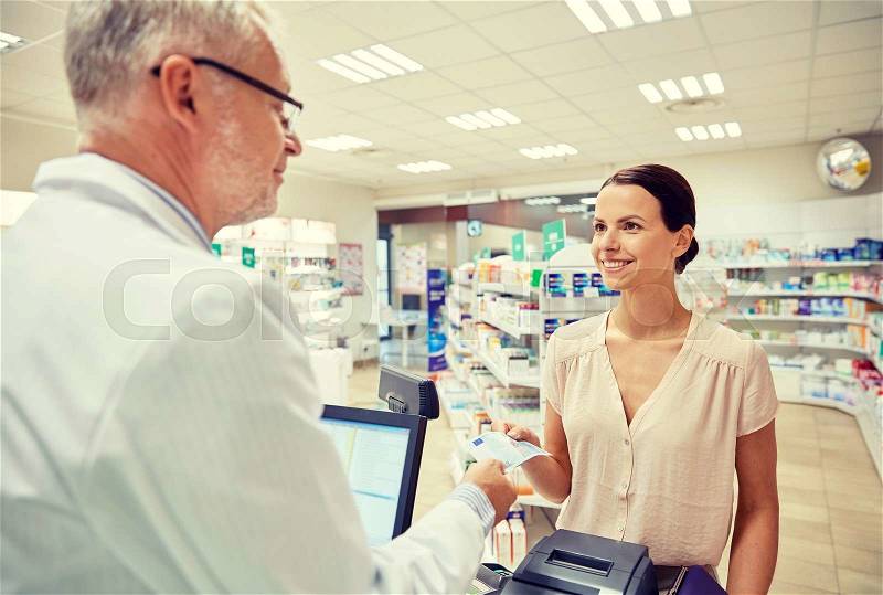 Medicine, pharmaceutics, health care and people concept - smiling woman with wallet giving money to senior man pharmacist at drugstore cash register, stock photo