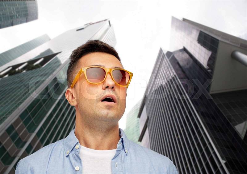 Summer, emotions, style and people concept - face of scared or surprised middle aged latin man in shirt and sunglasses over city skyscrapers background, stock photo