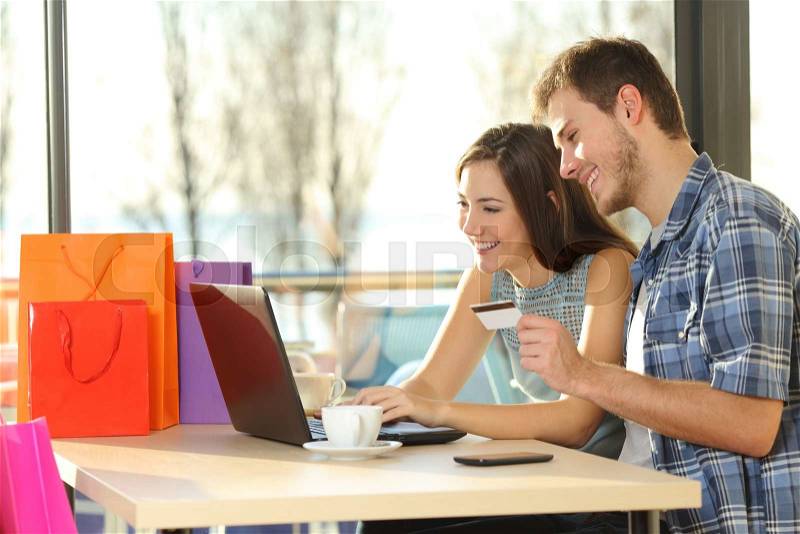 Couple buying online with credit card and laptop with shopping bags in a coffee shop, stock photo