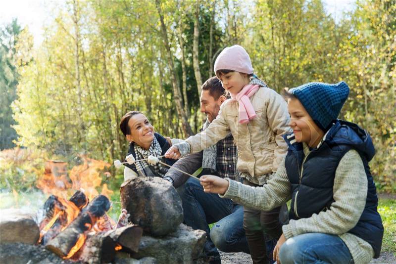 Camping, travel, tourism, hike and people concept - happy family roasting marshmallow over campfire, stock photo