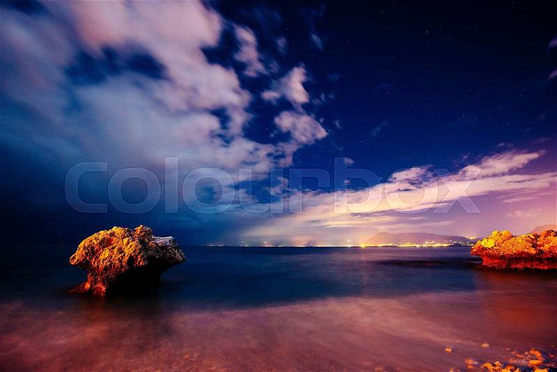 The starry sky above rocky mountains. Fantastic lighting city that appears in the sea, stock photo