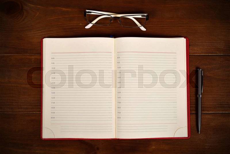 Open leather diary, glasses and pen on wooden desk, stock photo