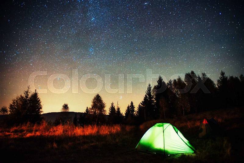 Camping under the stars. Green solo tent under dark night sky full of stars and constellations, stock photo
