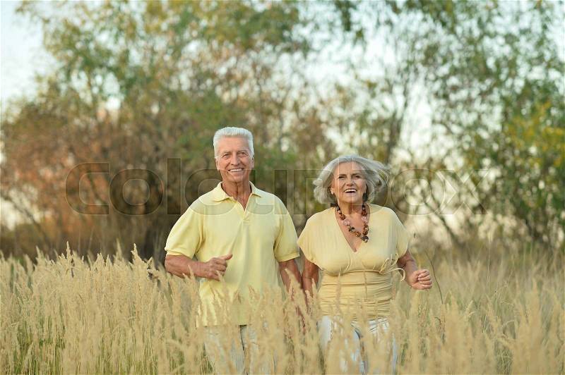 Beautiful happy senior couple running in summer field, stock photo