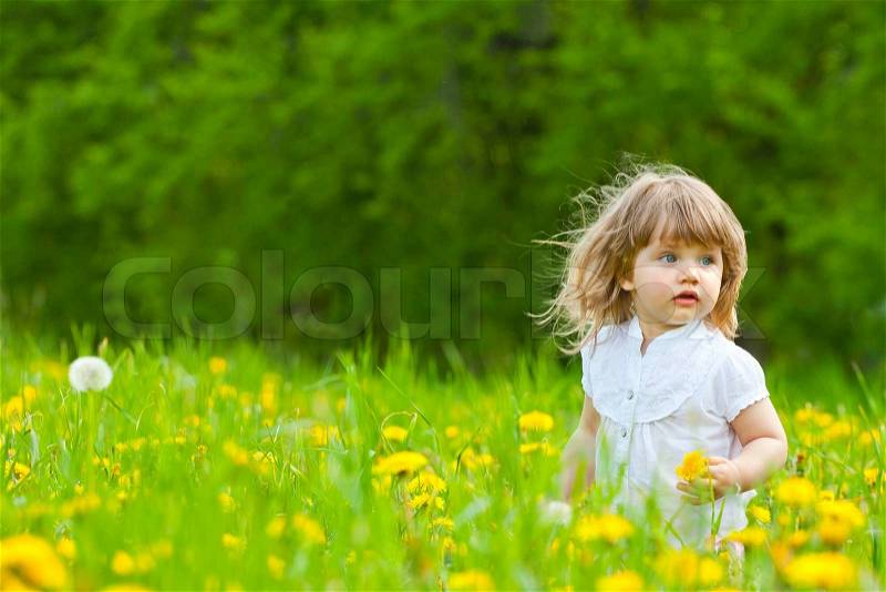 Little girl in a dandelion meadow showin with hand to the side, stock photo