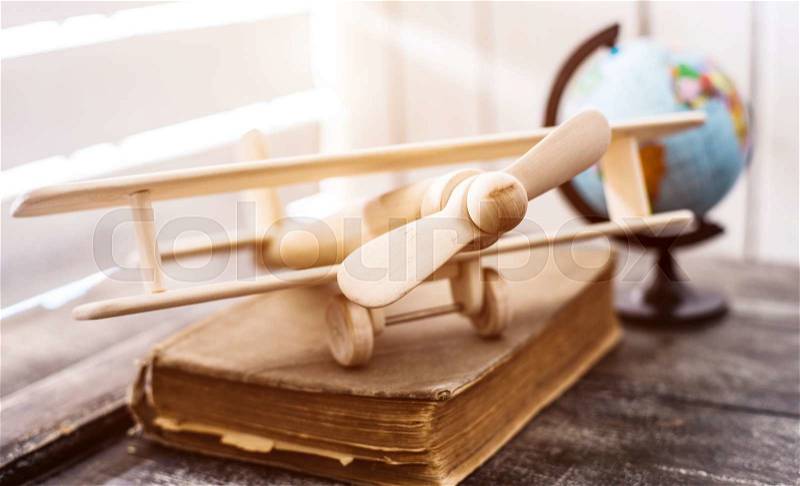 Beautiful handmade wooden toy-plane on a book with globe on the background, stock photo