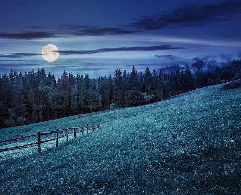 Autumn landscape. fence on the hillside meadow near forest in mountain at night in full moon light, stock photo
