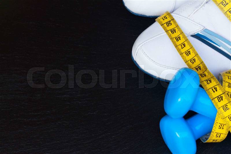 Training shoes with measuring tape, blue dumbbells border on black stone, stock photo