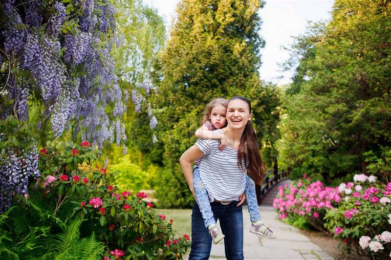 Mother and daughter walking in the summer park.Daughter was tired. Woman carries a child on his shoulders They are surrounded by beautiful flowering plants. Woman smiling. A pleasant holiday in nature, stock photo