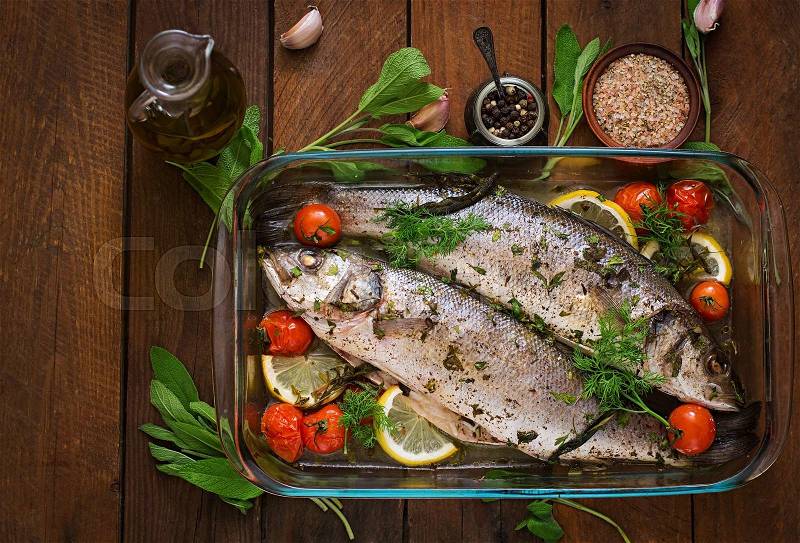 Two baked seabass in a baking dish with spices on an wooden background. Top view, stock photo
