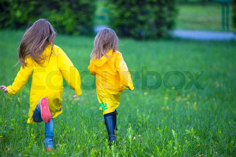 Funny cute toddler girls wearing waterproof coat playing outdoors by rainy and sunny day, stock photo