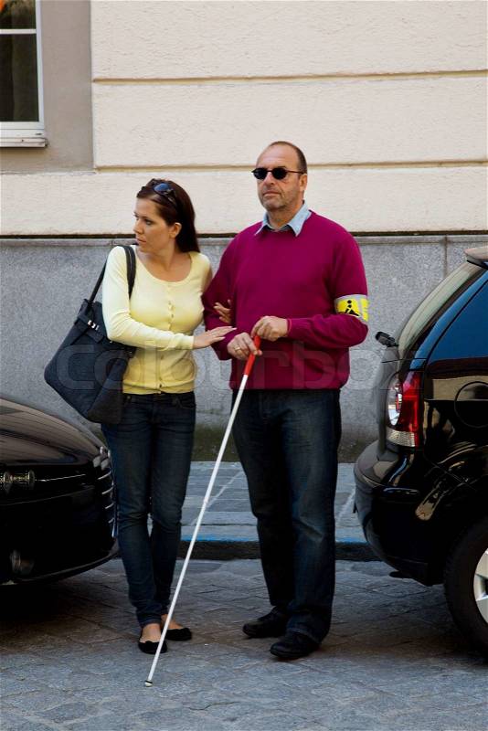 A young woman helps a man on the street blionden, stock photo