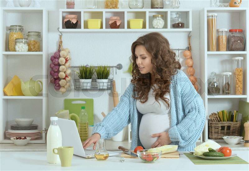 Beautiful pregnant woman with food at kitchen, stock photo