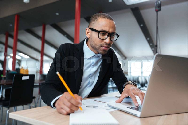 Young concentrated employee looking at computer monitor and noting during working day in office, stock photo