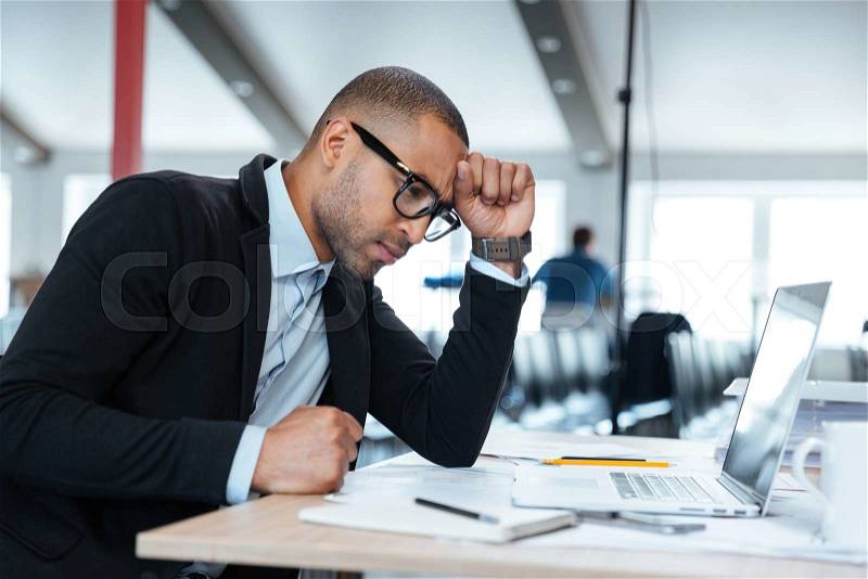 Serious smart businessman thinking about something using laptop in the office, stock photo