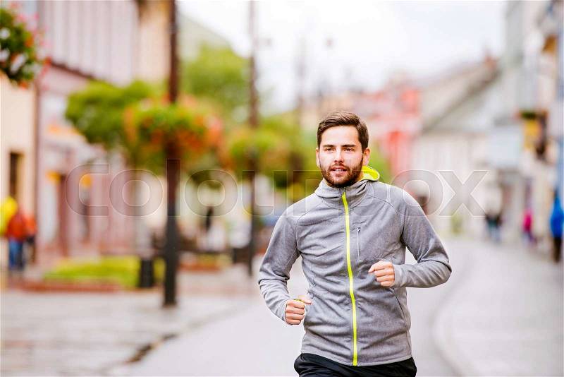 Young hipster man in gray sweatshirt running in town, main street, stock photo