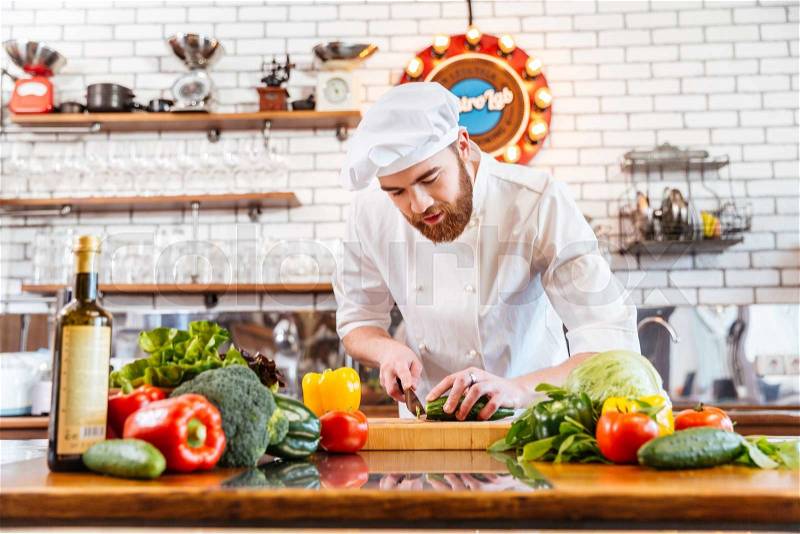 Concentrated attractive chef cook in uniform standing and cutting fresh vegetables for salad on the kitchen, stock photo