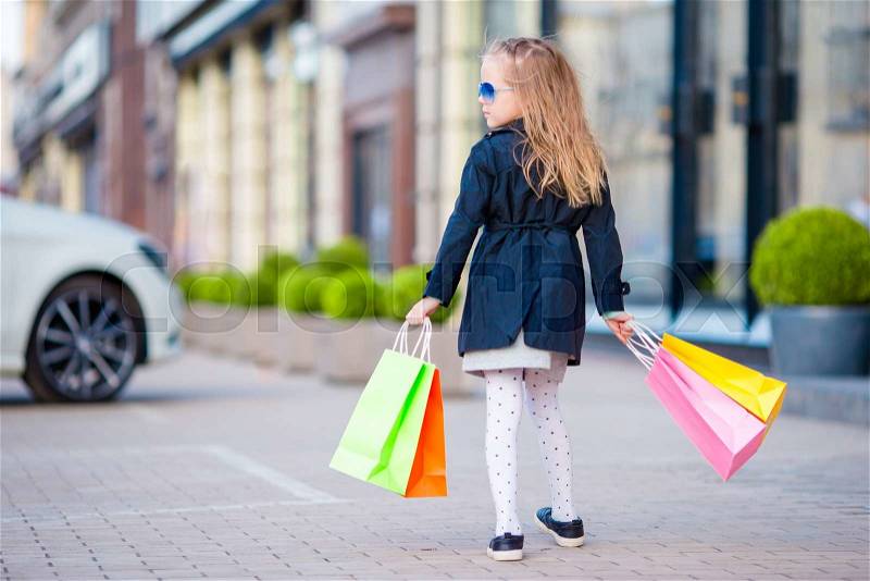 Adorable little girl having fun with shopping bags outdoors, stock photo