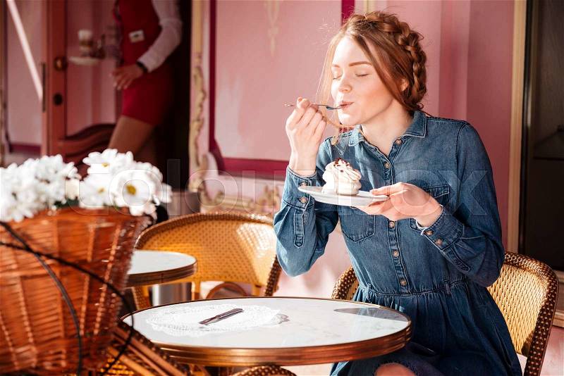 Relaxed pretty young woman sitting and eating cupcake in outdoor cafe, stock photo