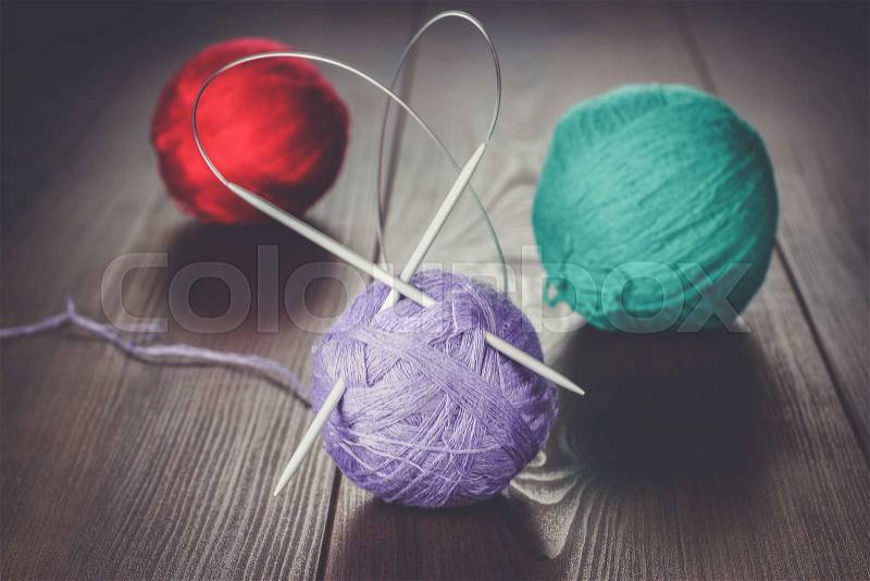 Knitting needles and balls of threads on wooden table, stock photo