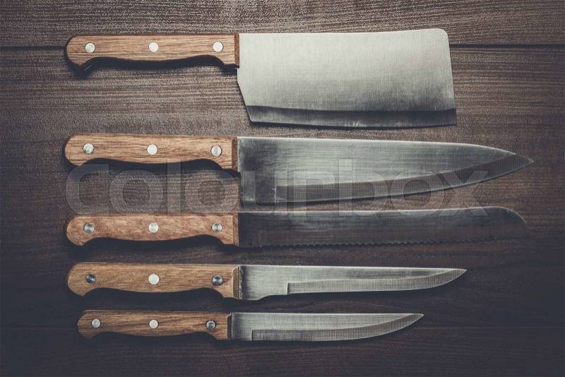 Five kitchen knifes over brown wooden table, stock photo