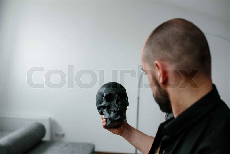 Handsome, bearded man holding a black skull, stock photo