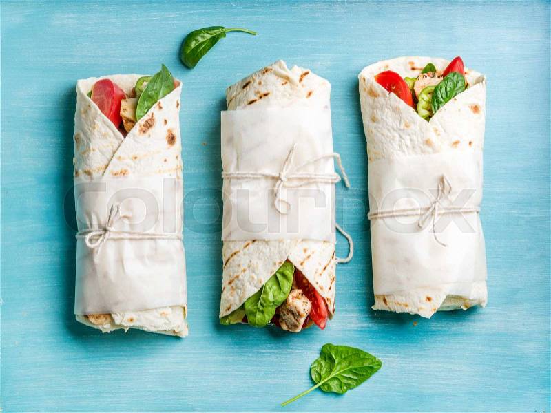 Healthy lunch snack. Tortilla wraps with grilled chicken fillet and fresh vegetables on blue painted wooden background. Top view, stock photo