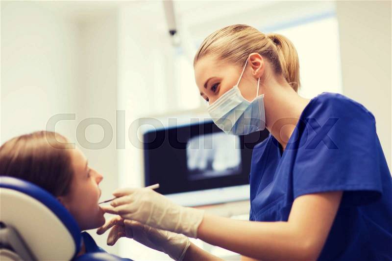 People, medicine, stomatology and health care concept - happy female dentist with mirror or dental probe checking patient girl teeth up at dental clinic office, stock photo
