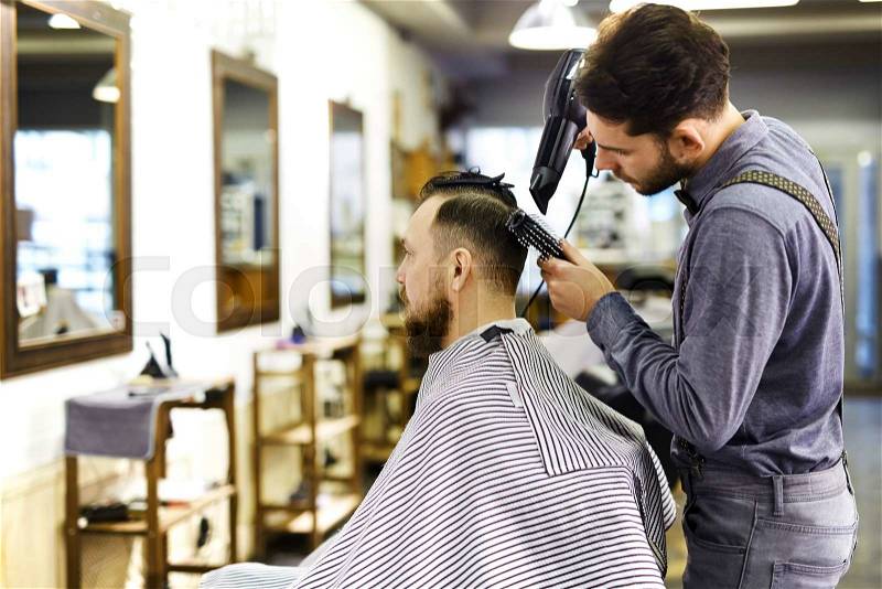 Young barber styling hair of his client, stock photo
