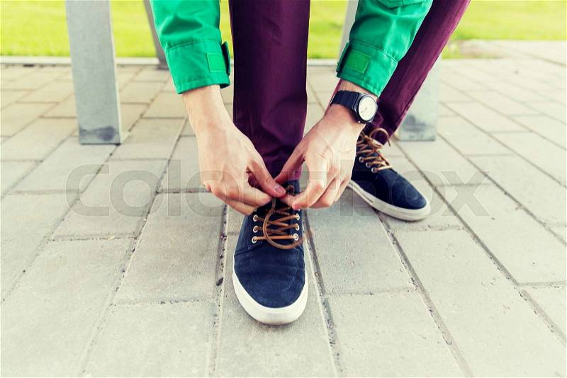 People, footwear and fashion concept - close up of male hands tying shoe laces on street, stock photo