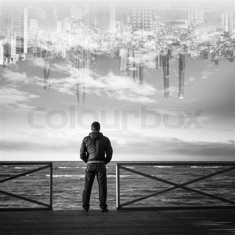 Young man starring on the sea with the city in the sky on a background. Rear view, black and white collage photo, stock photo