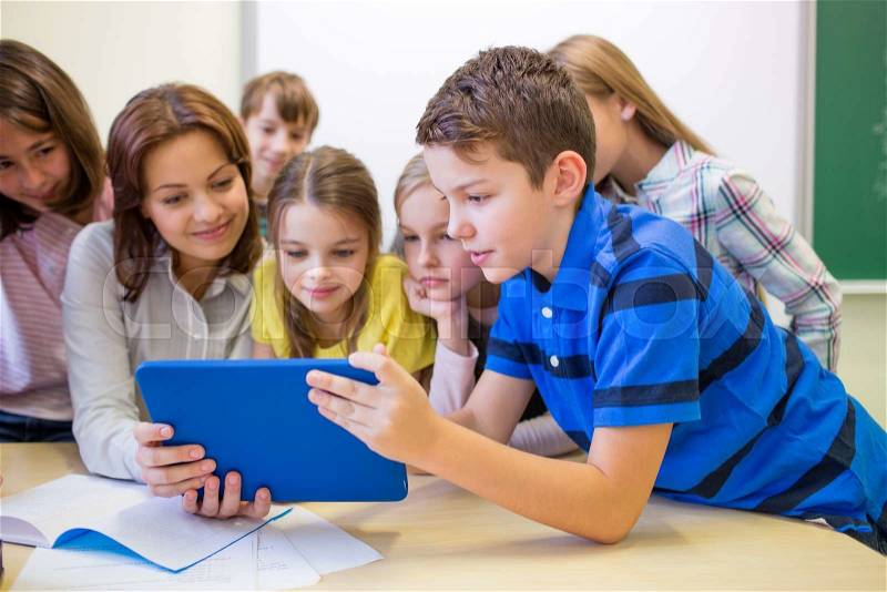 Education, elementary school, learning, technology and people concept - group of school kids with teacher looking to tablet pc computer in classroom, stock photo