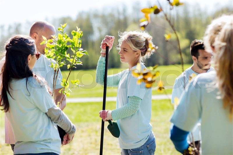 Volunteering, charity, people and ecology concept - group of volunteers with garden tools planting trees and talking in park, stock photo