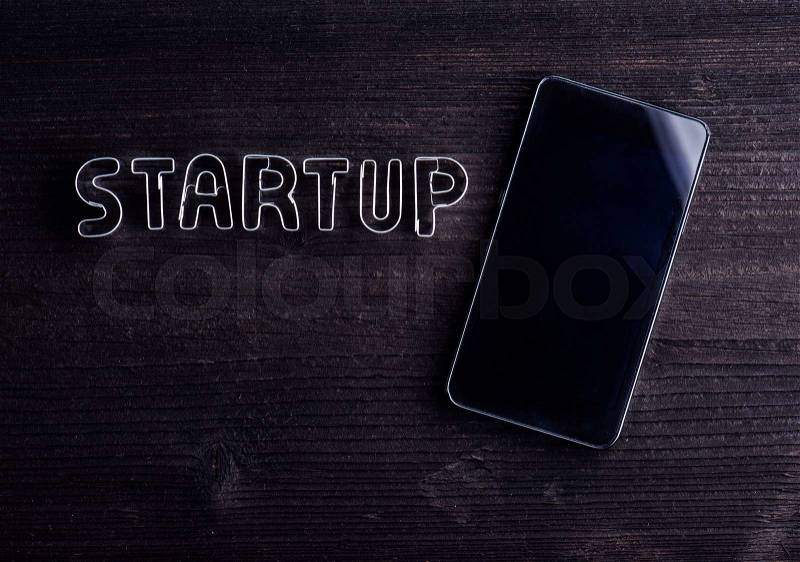 Smart phone and start up sign made of cookie cutters. Studio shot on dark wooden background. Flat lay. Copy space, stock photo