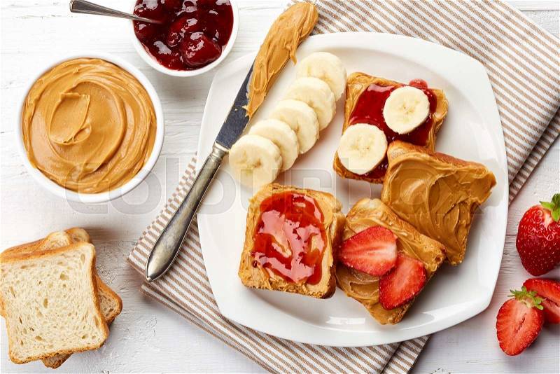 Plate of sandwiches with peanut butter, jam and fresh fruits from top view, stock photo