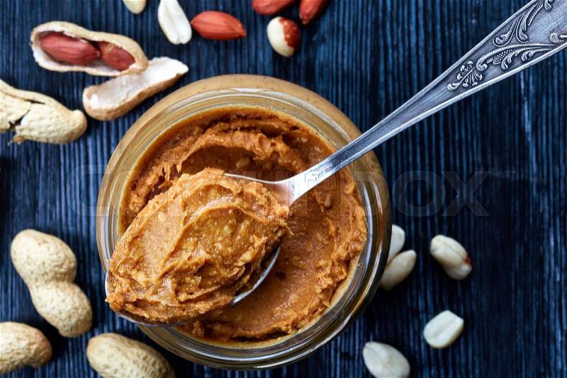 Jar and spoon of peanut butter and peanuts on dark wooden background from top view, stock photo