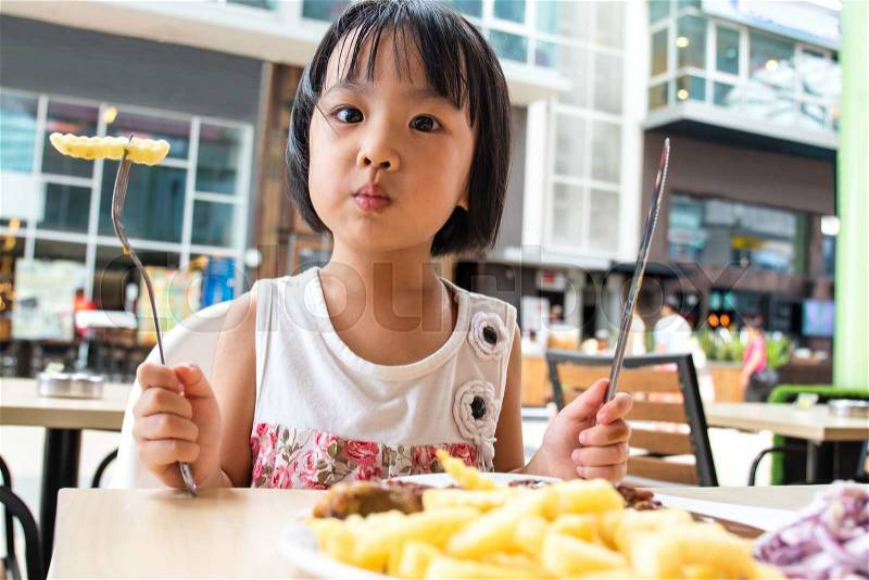 Asian Little Chinese Girl Eating Western Food in Outdoor Cafe, stock photo