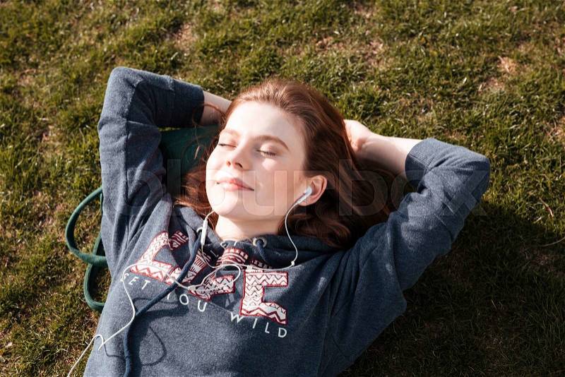 Top view of happy relaxed young woman lying on grass and listening to music, stock photo